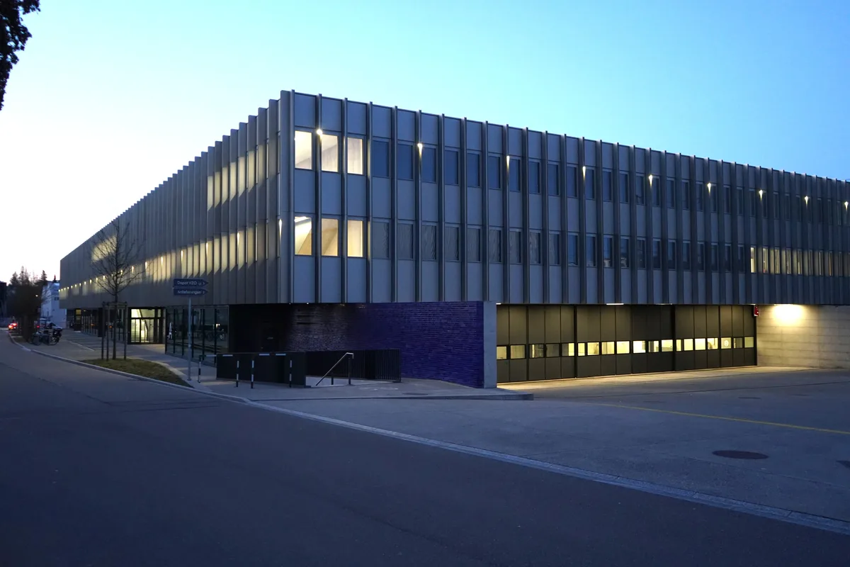 Das VZO-Depot in Wetzikon in der Abenddämmerung. Im Vordergrund sieht man grosse Einfahrtstore, darüber beleuchtete Fenster.